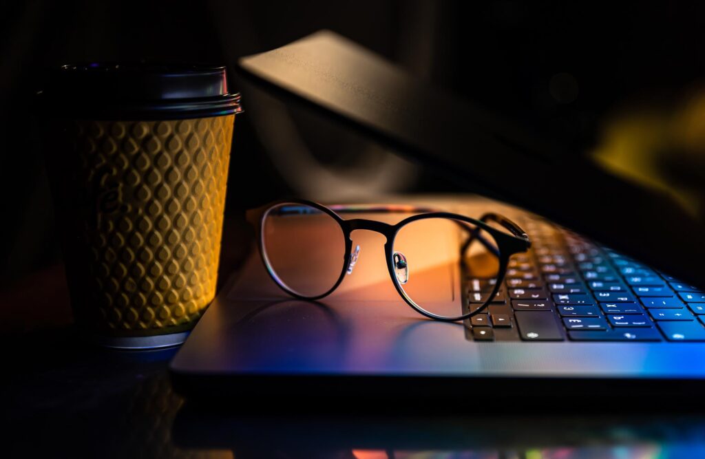 laptop half closed dark with colourful glow glasses paper cup